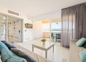 Salón luminoso de un apartamento moderno con sofá, mesa de centro, acceso al dormitorio y terraza con vistas al mar. Salón luminoso de un apartamento moderno con sofá, mesa de centro, acceso al dormitorio y terraza con vistas al mar.